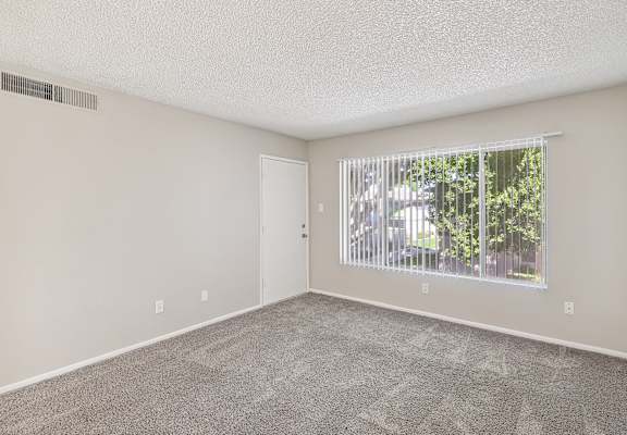 an empty living room with a large window and carpeting